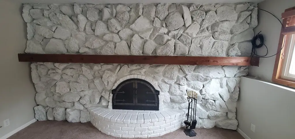 The same fireplace after: fieldstone and brick hearth painted white, the wood mantel left natural
