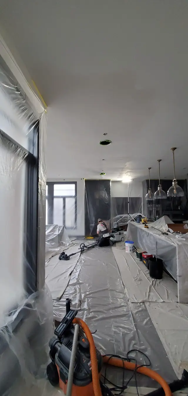 A room sealed in plastic sheeting with a worker sanding, face turned away