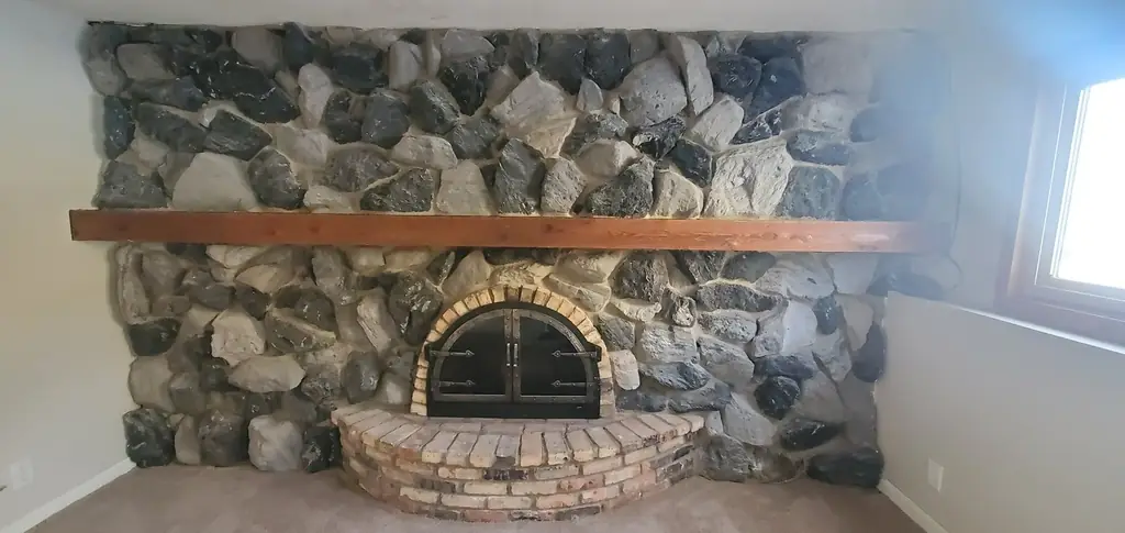 The fireplace before: grey and black fieldstone with a natural red brick hearth under a wood mantel